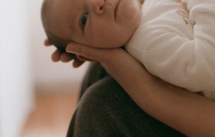 Tender close-up of a newborn baby being gently cradled, captured in soft natural light.